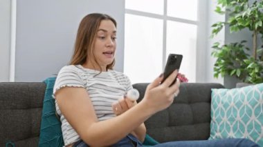 Endişeli genç kadın, kapalı koltukta akıllı telefon kullanırken reçeteli ilaç şişesini inceliyor..