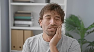 Modern ofis ortamında diş ağrısını ifade eden bir adam acı, sağlık ve kapalı mekan teması sergiliyor..