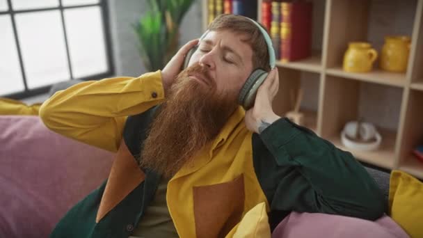 Zrelaksowany Brodaty Mężczyzna Słucha Muzyki Słuchawkach Leżąc Kolorowej Kanapie — Wideo stockowe