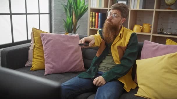 Bärtiger Mann Mit Brille Sitzt Drinnen Auf Sofa Vor Dem — Stockvideo