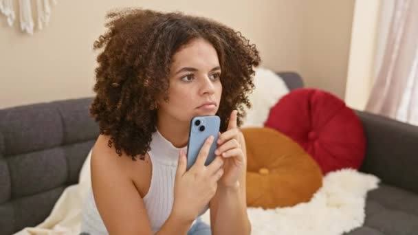 一位满头卷发 沉思的年轻女子在舒适的客厅里用智能手机 流露出一种美丽和体贴的感觉 — 图库视频影像