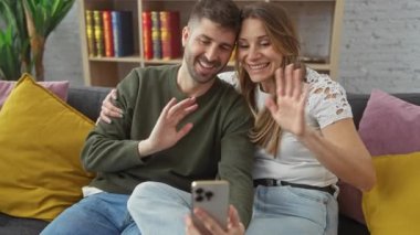 Gülümseyen bir adam ve kadın kanepede yakın otururlar, rahat, kitaplık dekore edilmiş oturma odasında selfie çekerler..