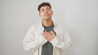 Neşeli genç Arap adam, günlük giysiler içinde, minnetle gülümseyen ve göğsünde el ele tutuşan, sağlığın ve dürüstlüğün sembolü, beyaz tenli. Mutlu, kendinden emin ve arkadaş canlısı yaşam tarzları yayar.