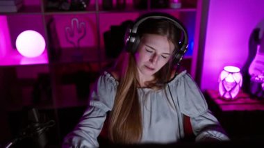 Kulaklık takan genç sarışın bir kadın geceleri neon ışıklarıyla aydınlatılan canlı bir oyun odasında mikrofonla meşgul oluyor..