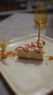 Nefis bir cheesecake, arkaplanda bulanık bir bardakla seramik tabakta canlı yenebilir süslemelerle süslenmiş..