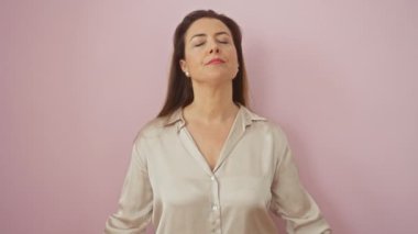 Rahatlamış İspanyol kadın zen pozuyla meditasyon yapıyor, sakin ışıldıyor, gözleri yoga konseptine kapalı. gömlekli, pembe arka planda izole edilmiş..