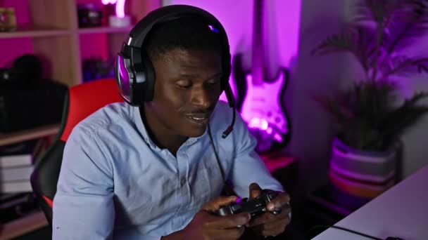 一个全神贯注的非洲男人 带着耳机 晚上在一个充满活力的家庭游戏室里玩电子游戏 — 图库视频影像