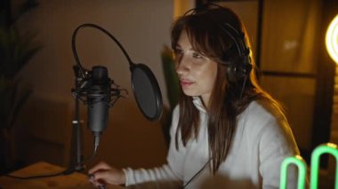 Genç bir kadın, kapalı bir müzik stüdyosunda, kulaklık takmış, tutkulu ve odaklı bir mikrofon kullanıyor..