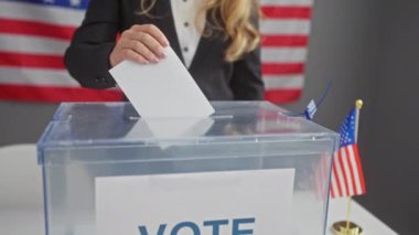 Beyaz bir kadın, bayraklarla süslenmiş bir Amerikan seçim merkezinde oy kullanıyor..