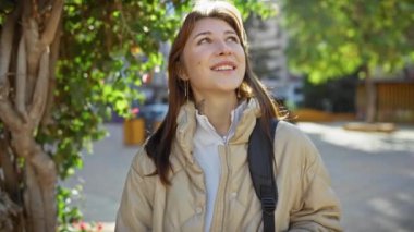 Genç bir kadın doğal olarak gülümsüyor, güneşli bir günün tadını çıkarıyor, şehir parkında, öylesine bir zarafet yayıyor..
