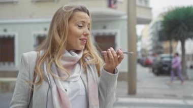 Açık hava ortamında telefonuna sesli mesaj gönderen gülümseyen beyaz bir kadın.