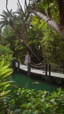 Güzel genç bir kadın, yemyeşil ve koi balıklarıyla çevrili huzurlu bir bali tatil köyünde geziniyor..
