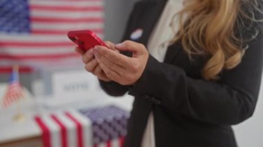 Takım elbiseli genç sarışın bir kadın oy verme merkezinde Amerikan bayrağı olan bir akıllı telefon kullanıyor.