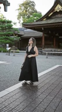 Kendinden emin bir şekilde Fushimi Inari Taisha 'ya poz veriyor, gözlüklü güzel bir İspanyol kadın, geniş bir şekilde gülümsüyor, etrafına bakıyor, büyüleyici Kyoto tapınağı çevresinden büyüleniyor..