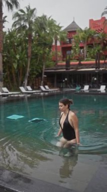 Genç bir kadın, tropikal yeşilliklerle çevrili lüks bir bali tatil köyünün açık havuzunda huzurlu bir anın tadını çıkarıyor..
