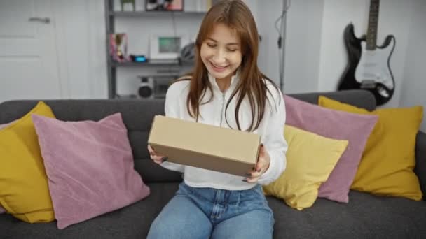 笑顔の若い女性がモダンなリビングルームの居心地の良い内装の小包箱を調べる — ストック動画