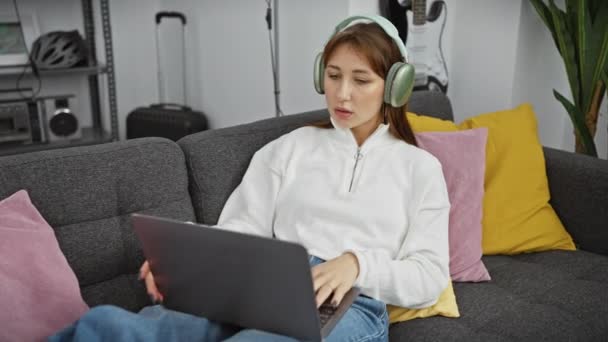 Uma Jovem Mulher Usando Fones Ouvido Usa Laptop Sofá Uma — Vídeo de Stock