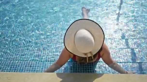 一个女人躺在度假胜地的游泳池边 戴着宽边帽 让人想起一个宁静的夏天 — 图库视频影像