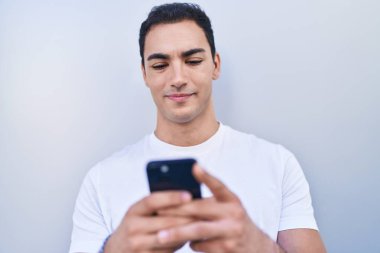 Genç İspanyol adam kendine güvenen, izole edilmiş beyaz arka plan üzerinde akıllı telefon kullanan.