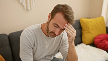 Orta yaşlı, sakallı, ispanyol bir adam rahat bir oturma odasındaki kanepede otururken sıkıntılı görünüyor..