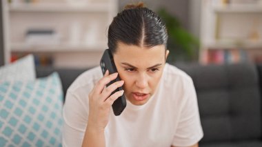 Genç ve güzel İspanyol kadın evde üzgün bir şekilde akıllı telefondan konuşuyor.