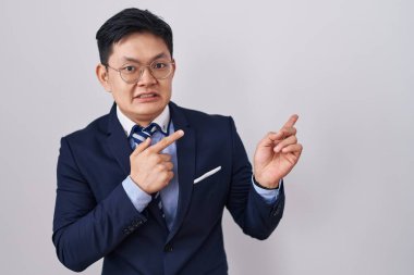 Genç Asyalı takım elbiseli ve kravatlı bir adam endişeli ve gergin bir tarafı işaret ediyor, endişeli ve şaşırmış bir yüz ifadesi var. 