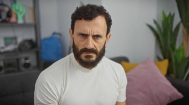 Ciddi orta yaşlı sakallı bir adam modern bir oturma odasında oturur ve tefekkür havasını iletir..