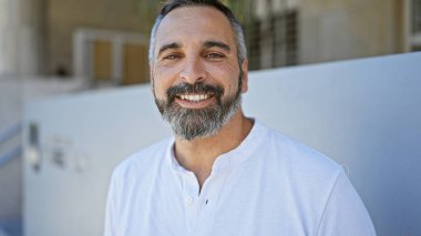 Gülümseyen sakallı, olgun İspanyol bir adam. Sıradan bir tarzı ve şehirli bir geçmişi var.