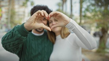 A couple forms a heart with their hands on an urban street, symbolizing love and togetherness in a city setting. clipart