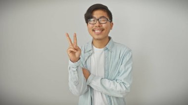 Neşeli genç Asyalı bir adam beyaz tenha bir geçmişi olan barış işareti yapıyor.