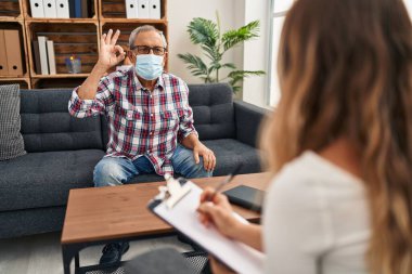 Tıbbi maskeli neşeli kıdemli adam parmağıyla 