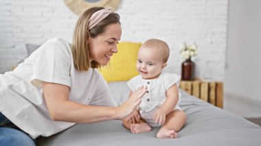 Kendine güvenen anne ve kız çocuğu, mutlu bir anı paylaşıyorlar, rahat bir yatak odasında birlikte oturuyorlar, sevgi ve mutluluğun tadını çıkarıyorlar. Gülümseyen yüzleri odada olumlu bir hava yayıyordu..