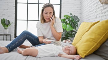 Yorgun anne yatak odasındaki hasta kızın ateşini kontrol ederken telefonda konsültasyon yapıyor.