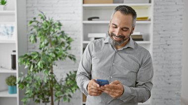 Gülümseyen yaşlı, gri sakallı adam modern ofiste akıllı telefon kullanıyor..