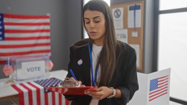 İspanyol kadın, bayraklarla süslenmiş bir Amerikan seçim merkezinde notlar alıyor.