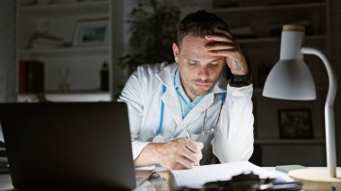 Geceleri hastane ofisinde sakallı, yorgun İspanyol bir doktor uzun bir iş gününü yansıtıyor..