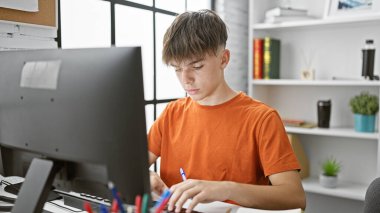 Focused teenage boy studying at a modern home desk setup, with a computer and notebooks clipart