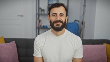 Modern bir oturma odasında gülümseyen sakallı, orta yaşlı yakışıklı bir adam..