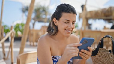 Genç İspanyol kadın mutlu bir şekilde gülümsüyor. Sunny restaurant terasındaki masada oturuyor.