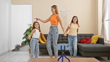 Genç bir kadın ve iki kız oturma odasında neşeyle dans ediyor, akıllı telefondan bir video kaydediyorlar..