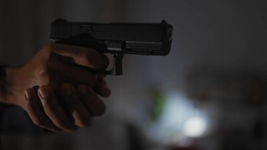 Silah odaklı bir tabanca tutan tanımlanamayan bir erkeğin yakın plan görüntüsü şüpheli bir kapalı mekan senaryosu olduğunu gösteriyor..