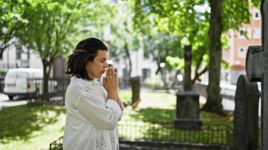 Güzel, genç, İspanyol bir kadın mezarlıkta dua ediyor ve yas tutuyor.