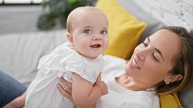 Neşeli anne yatakta uzanıyor, yatak odasında güzel gülümseyen kızına sarılıyor, ev ortamında sevgisini ifade ediyor.