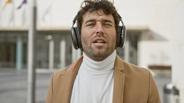 Sakallı genç bir İspanyol, şehir caddesinde dururken kulaklıkla müzik dinlemekten hoşlanıyor..