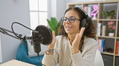 Gülümseyen İspanyol kadın radyo stüdyosunda mikrofonla kayıt yapıyor..