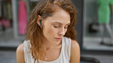 Kulaklıklı, şehir caddesinde oturan, şehir yaşam tarzını ve tefekkür etmeyi özetleyen düşünceli, genç beyaz bir kadın..