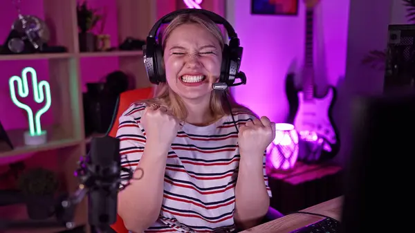 stock image Excited young woman with blonde hair celebrating a victory in a neon-lit gaming room at night.