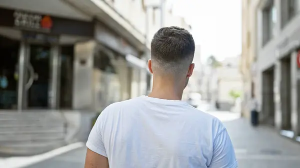 stock image Back view of a young, hispanic man in casual clothing standing on an urban city street during daytime.