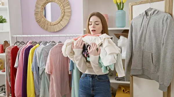 stock image A young woman struggles with an armful of clothes in a colorful, organized dressing room.