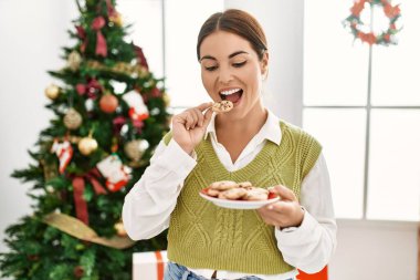 Genç ve güzel İspanyol kadın evde Noel ağacının yanında kurabiye yiyor.